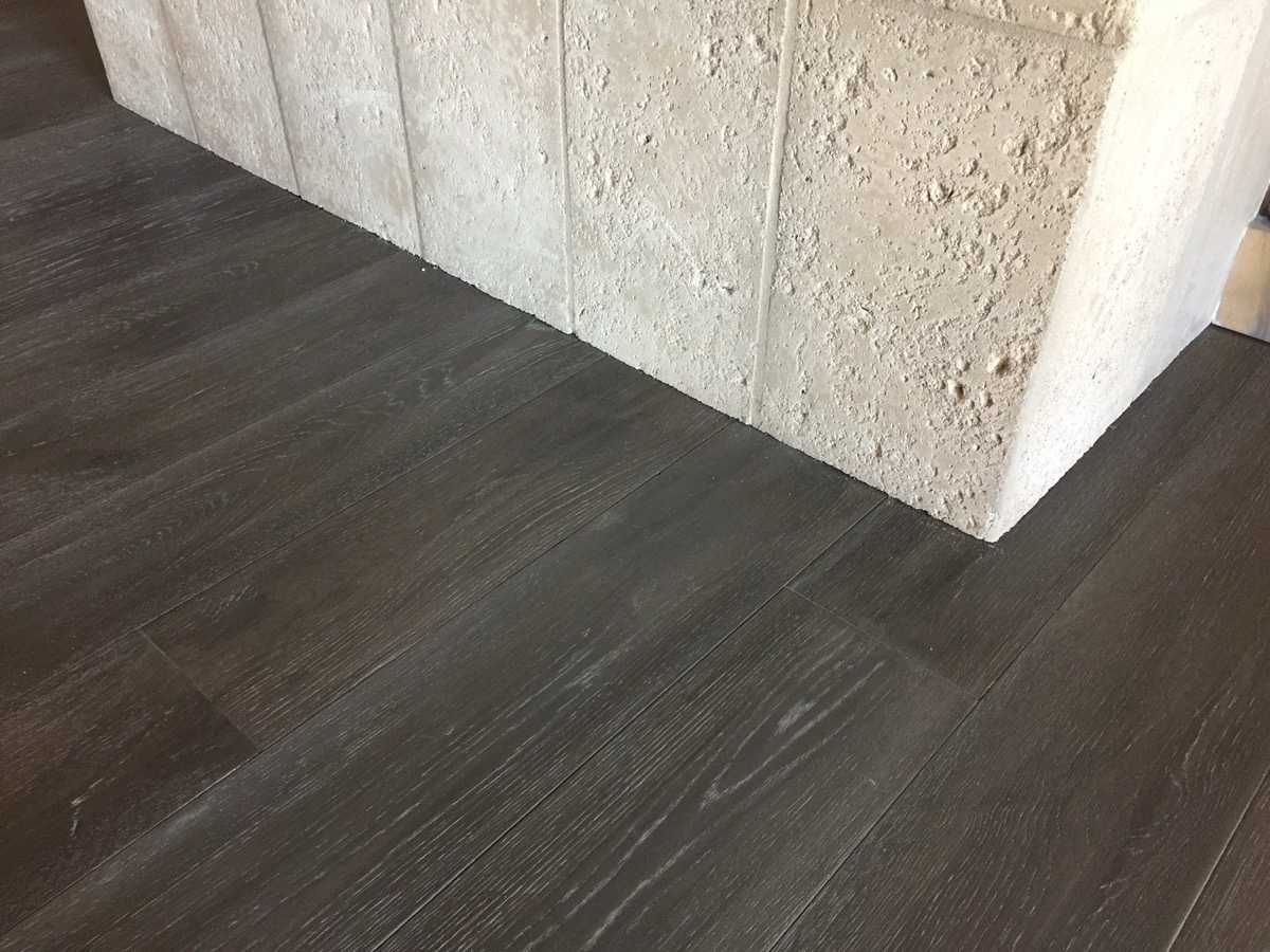 Dark hardwood plank floor beside a travertine column